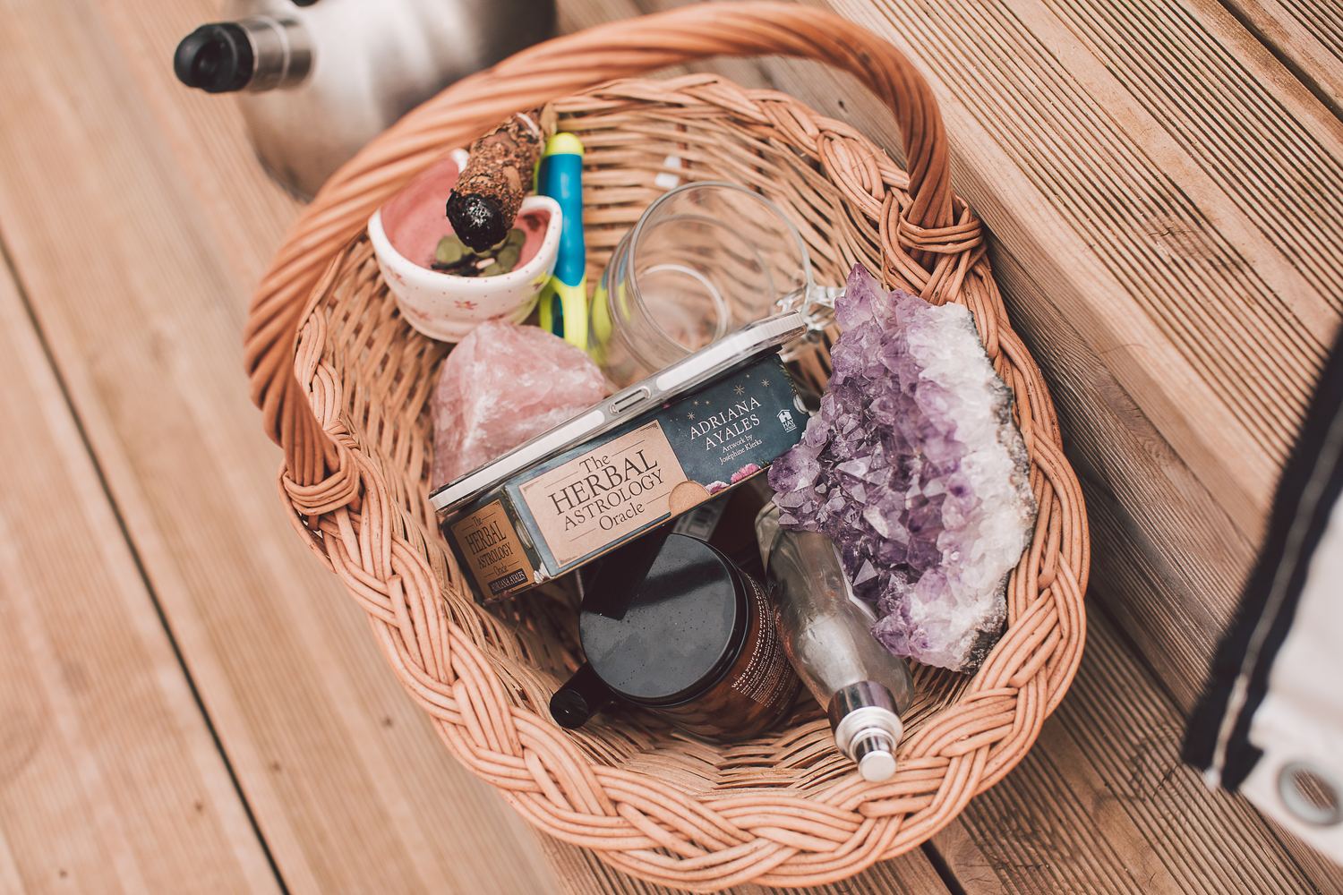 A woven basket holding oils, crystals, oracle cards and a jar of balm
