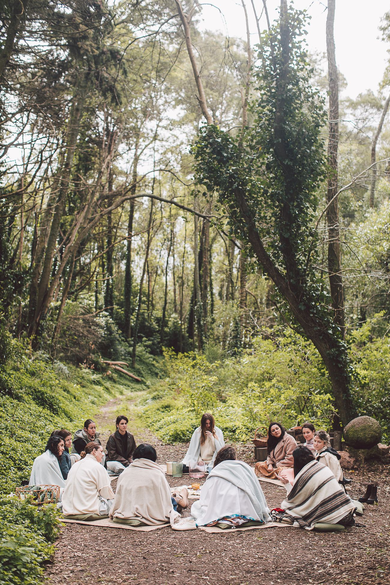 Women sitting in circle in the forest, wrapped in blankets